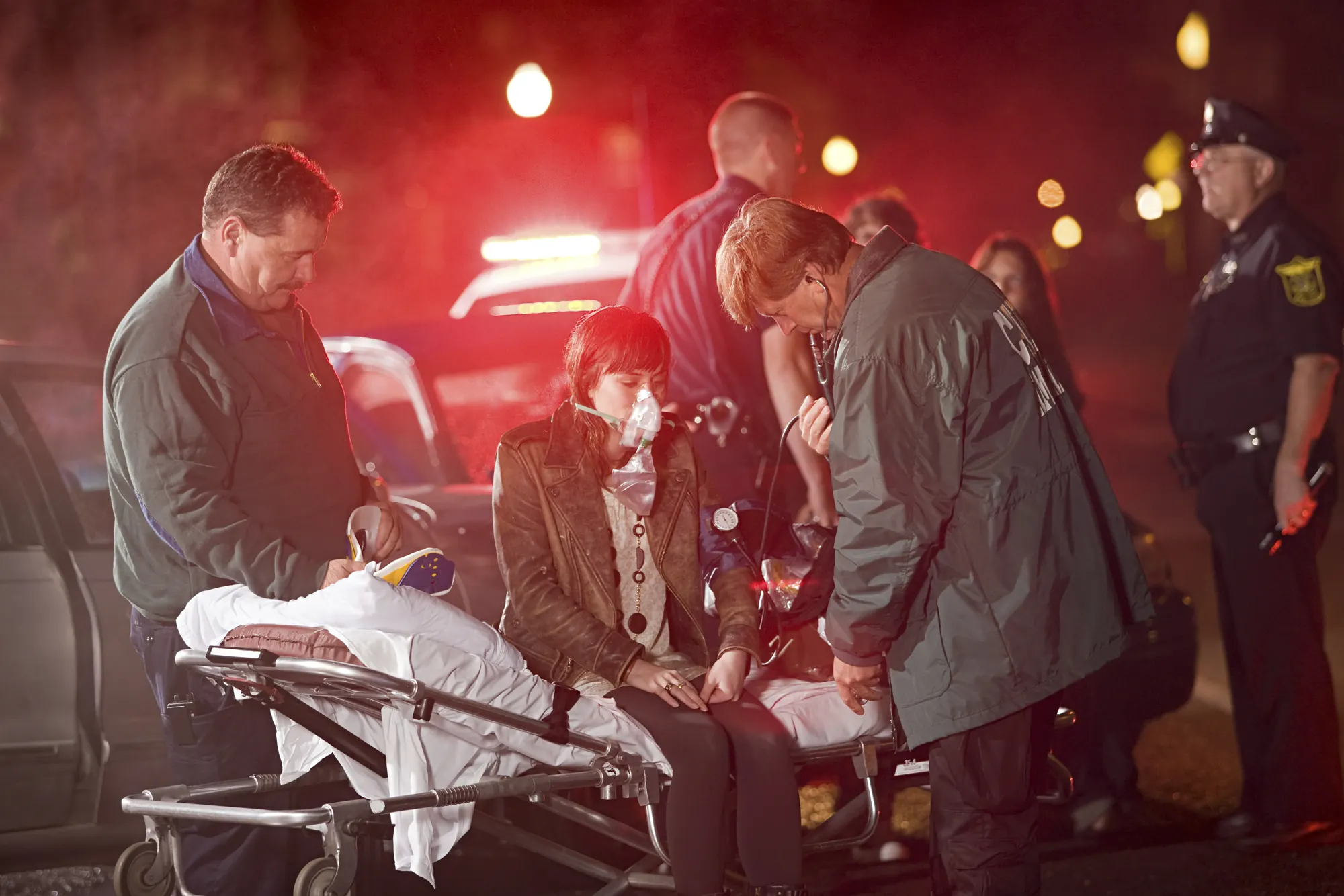 Paramedics and police officers attending an injured woman on an oxygen mask at the scene of an accident