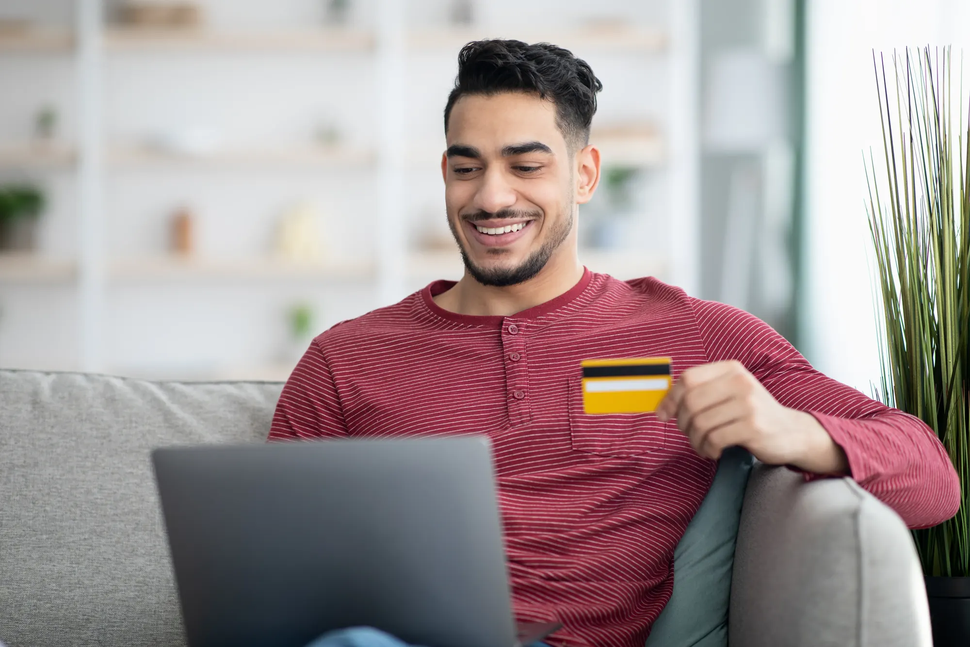Smiling man holding a credit card with a laptop, rebuilding his credit